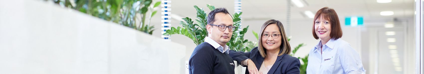 온라인슬롯사이트 직원 3명이 사무실에 서있습니다. 왼쪽에 남자 한 명, 오른쪽에 여자 두 명